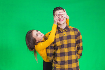 Playful girl covering boyfriend's eyes with hands on green background.