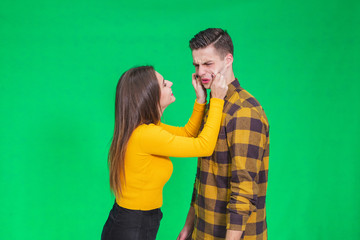 Girl pinching guy's cheeks, making fyn, he is scowling his face, looking completely annoyed.