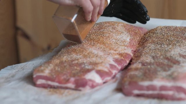 Applying red pepper rub to raw pork meat preparing for barbecue smoking wearing a black rubber glove