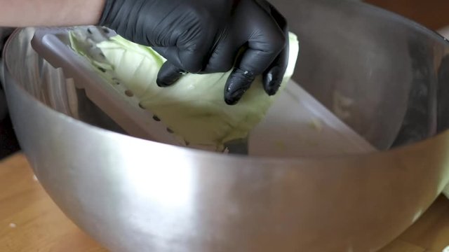Cutting cabage using a mandoline preparing coleslaw salat for barbeque wearing a black rubber glove