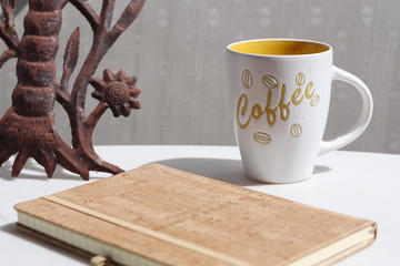 Yellow and white coffee mug on a table with a journal