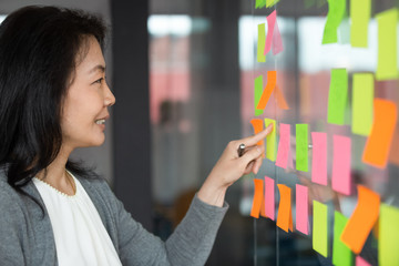 Smiling Asian businesswoman reading information on sticky papers