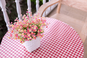 plastic flowers in white flower vase on the table decorated near the garden