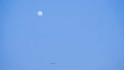 Evening moon with plane passing from a distance