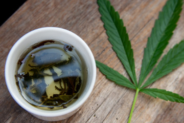 Green marijuana leaves and marijuana tea placed on an old wooden table.
