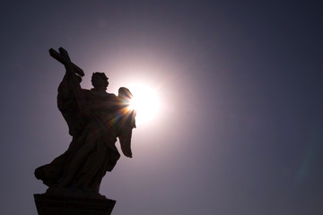 Marble statue at sunlight of Angel with the Cross, one of the ten angels on Saint Angel Bridge, symbols of Christ's Passion, Rome, Italy
