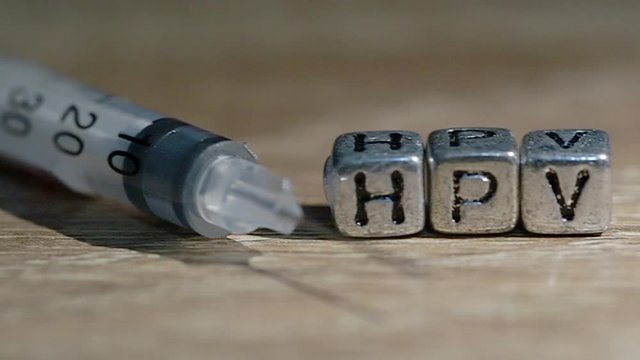 Injection needle with  Text " HPV"  put on wooden background. Concept Prevent HPV infection by vaccination before getting infected.