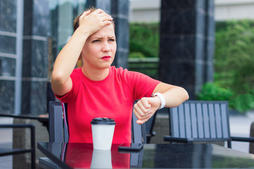 Beautiful sad upset nervous girl holding head with hand, remembered she forget or forgotten something to do. Young woman in a hurry, does not have time, looks at the watch, checks time. Cafe, coffee.