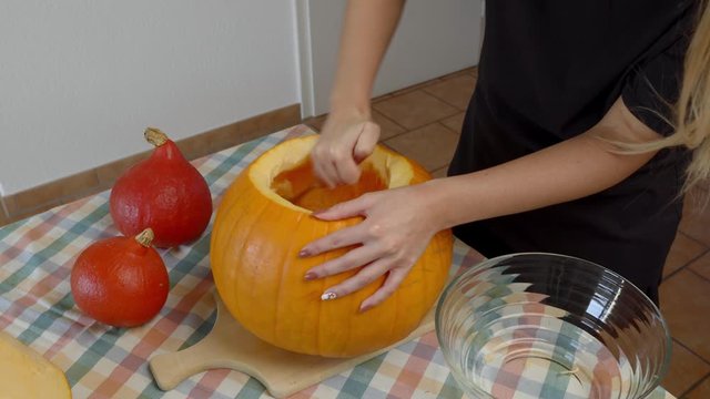 A Lady Using Spoon To Scrape The Seeds From Pumpkin for Carving - close up shot