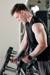 Plakat Fit young man choosing weight of dummbell to exercises with in gym