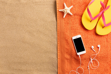 Summer vacation composition. Flip flops, smartphone and seashells on sand background