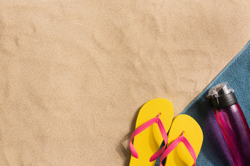 Top view flip flops and water bottle with copy space. Traveler accessories on sand. Travel vacation concept. Harsh light with shadows. Border composition made of towel
