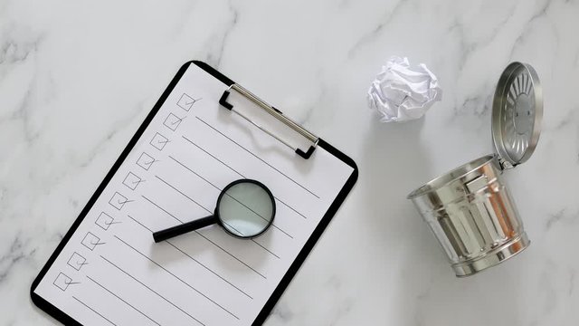 creative block or burnout, hand placing scrunched paper draft next to garbage bin and to do list on clipboard on business desk