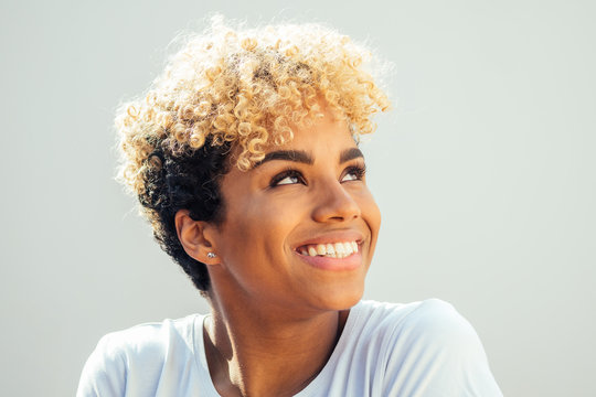 hispanic latin woman with afro blonde haircut dressed in white top looking up with charming shy smile in studio white background