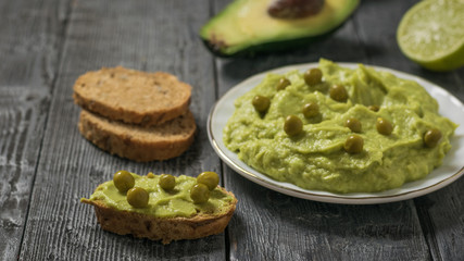 Whole-grain bread with guacamole and green peas on a black wooden table. Diet vegetarian Mexican food avocado.
