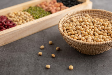 Soybean and grains in the wooden basket and in the wooden tray placed on the black cement floor. High angle view.