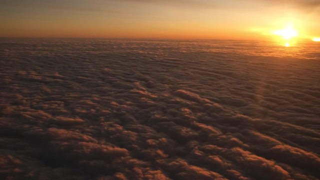 View from plane window sunshine clouds. Looking through window aircraft during flight in wing at sunset or sunrise. Clouds, sun and sky through window of airplane. Travel tourizm trip. 4 K slow-mo