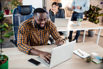 Positive delighted dark-skinned male person typing message