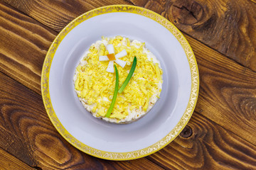 Traditional russian layered salad Mimosa with spring decoration Daffodil. Decoration is made of egg, green onion and carrot. Top view