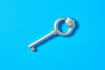 Single old antique silver key lies on blue color desk. Top view. Close-up