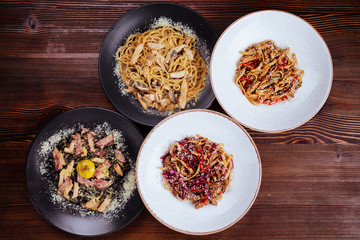 Several plates of pasta with different kinds of sauce over wooden background, top view. Concepts of Italian food.