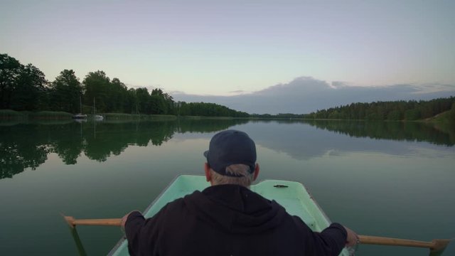 Man sitting in rowing boat on calm lake, rear wide shot, Suwalszczyzna, Poland