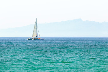 Obraz premium Sailboat in the sea in the sunlight over beautiful mountains background. Freedom concept.