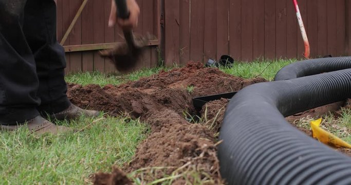 Worker digging out a trench to fit a new french drain pipe system in the ground