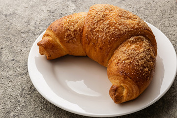 Croissant lies on a white plate. The plate is on a gray background.