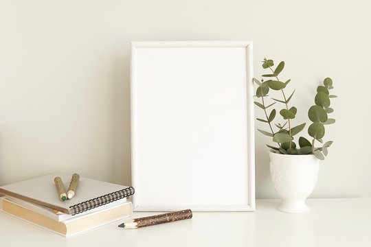 White frame mock up for poster, print, painting, minimal interior, eucalyptus branches, books, wooden pencils.