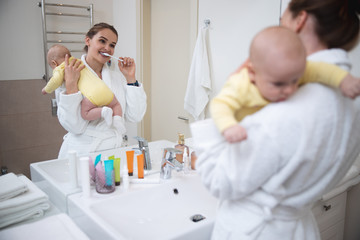 Obraz na płótnie Canvas Happy woman brushing teeth with her baby in arms stock photo