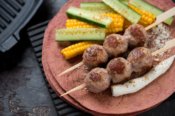 Close-up of roasted meatball skewers, sweet corn and cucumber on tortilla flatbread, studio shot