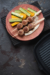 Wooden skewers with roasted meatballs, vegetables and tortilla flatbread, top view on a brown stone background with space