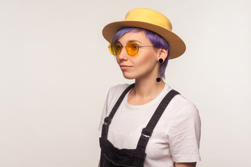 Fashion look. Half-turned portrait of glamour cute hipster girl with violet hair in sunglasses and hat looking aside, bright stylish appearance, clean skin. isolated on white background, studio shot