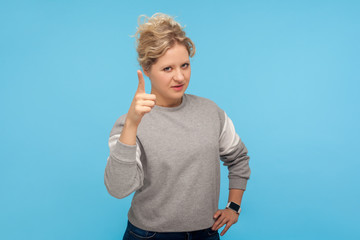 Be careful! Serious angry woman with short curly hair in sweatshirt warning with raised finger, admonishing gesture, blaming you for mistake, scolding. indoor studio shot isolated on blue background