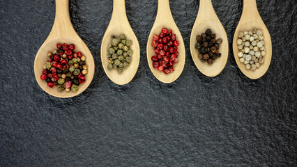 Wooden spoon with Pepper seeds on black stone background.