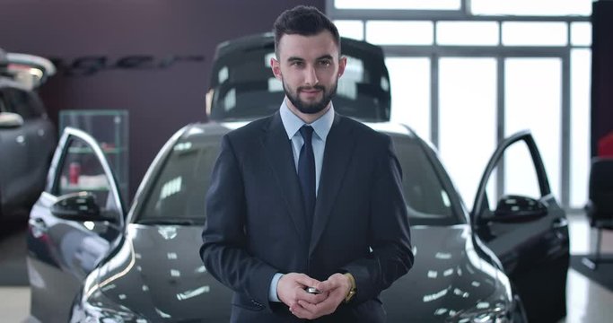 Portrait of young positive Caucasian man throwing up car keys and smiling at camera. Successful businessman purchasing new vehicle in dealership. Automobile industry, buying. Cinema 4k ProRes HQ.