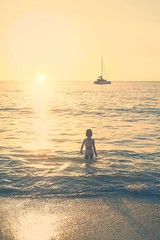 young girl in sea waves looks at boat and sunset. beautiful relax sea landscape. atmosphere summer vacation concept. 