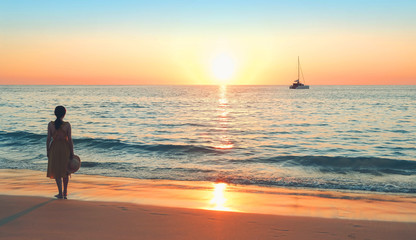 Fototapeta premium Young woman on beach sea and looking to a sun and ship. atmosphere seascape with Sunset and girl silhouette. dreamy, romantic relax image, vacation travel concept. copy space