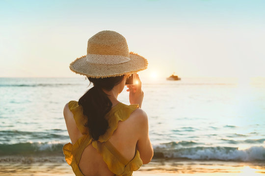 women on sea beach. girl in hat with phone a photographs of sunset on sea. Beach vacation, travel, summer concept. 