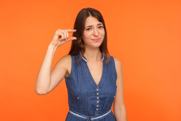 Small scale. Positive brunette woman in denim dress showing a little bit gesture and looking with...