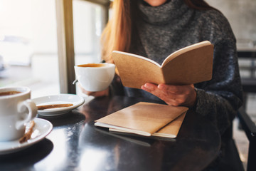 Closeup image of a woman reading a book while drinking coffee in cafe