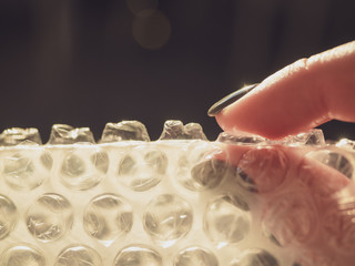 Fototapeta na wymiar A woman's hand bursts bubbles on a packaging bubble wrap, close-up. Burst the bubbles with your fingers to relieve stress, save space