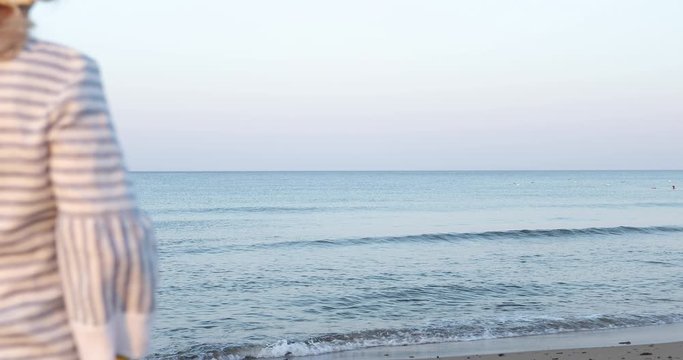 An elderly woman in straw hat standing on sea beach in the early morning.