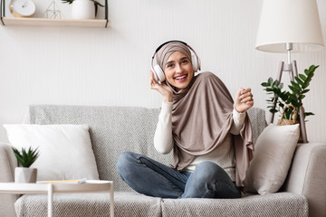 Obraz premium Arab girl sitting on sofa and listening music with wireless headphones