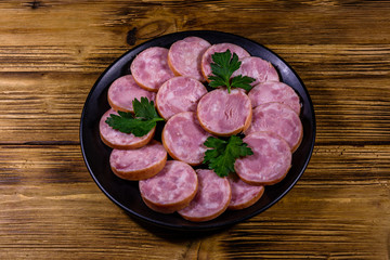 Black plate with sliced sausage on a wooden table