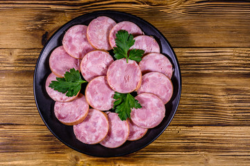 Black plate with sliced sausage on a wooden table. Top view