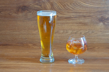 composition of alcoholic drinks with glass of whiskey and glass of clear beer on stage of oak tables
