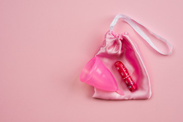 Pink  menstrual cup  and tampon lying on a silk bag isolated on a pink background.  Concept  critical days