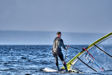 A male athlete is interested in windsurfing. He moves on a Sailboard on a large lake on an autumn...